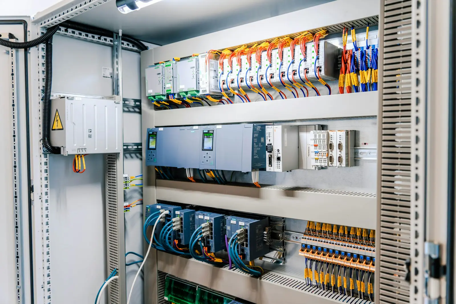 Open control panel with PLC modules, power supplies, network switches and labelled terminal wiring